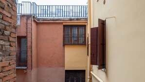 Un carrer estret amb una paret de maó d'un costat i una paret groga de l'altre. Hi ha una finestra amb reixes i una porta amb manilla.