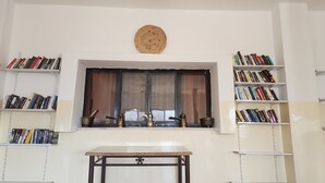 Una stanza con una finestra, due librerie, un tavolino e un arazzo.