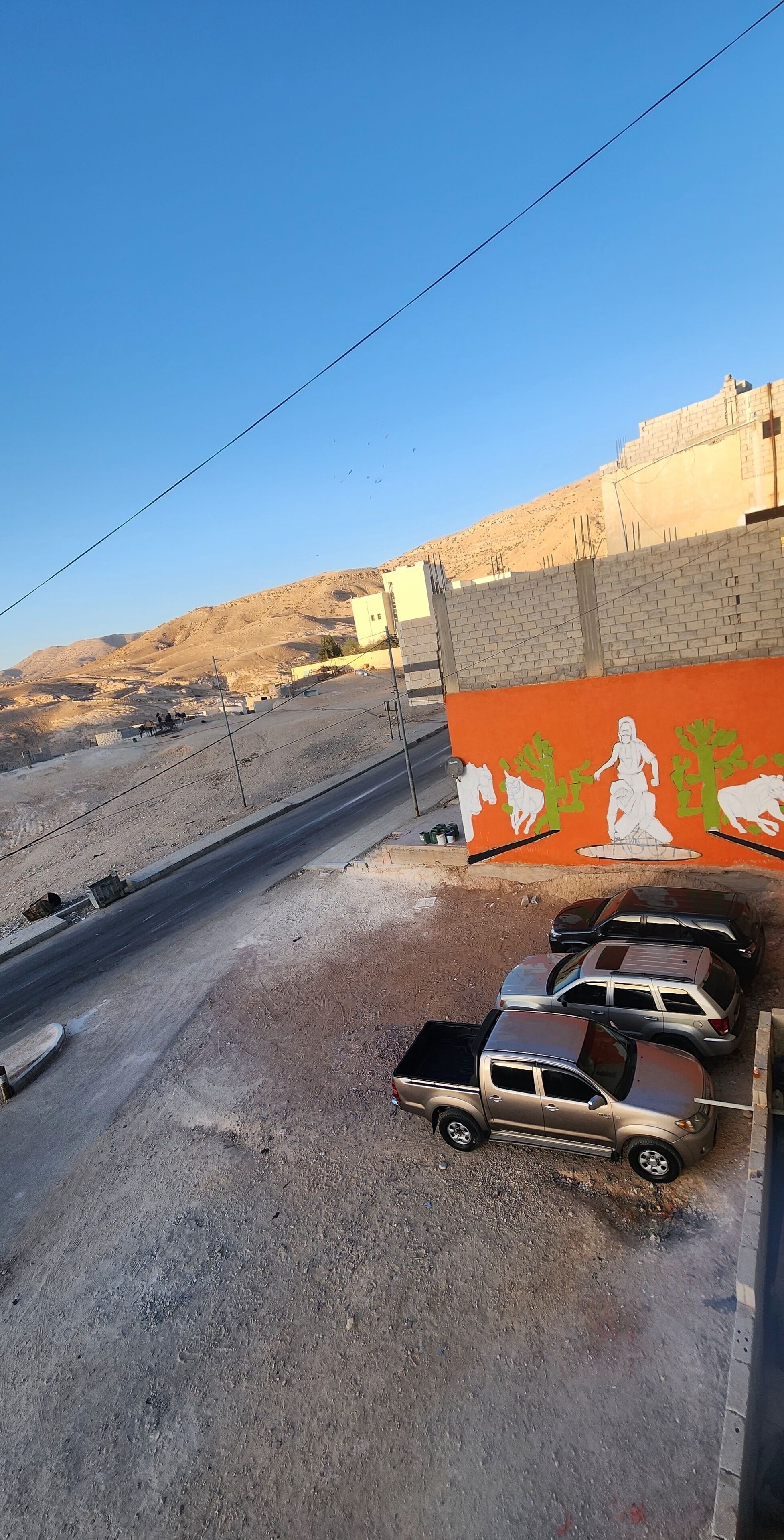 A parking area with several vehicles, a road, and a building with a mural.