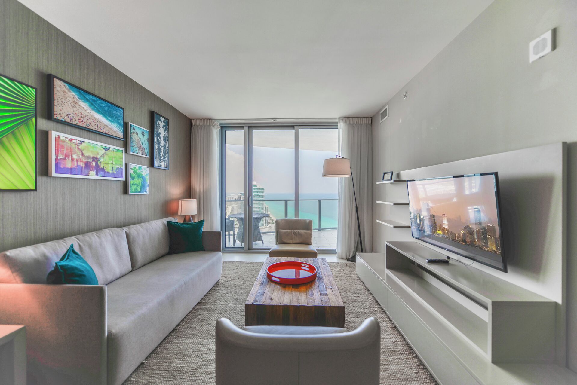 A modern hotel room with a sofa, a coffee table, a TV, and a balcony with a city view.