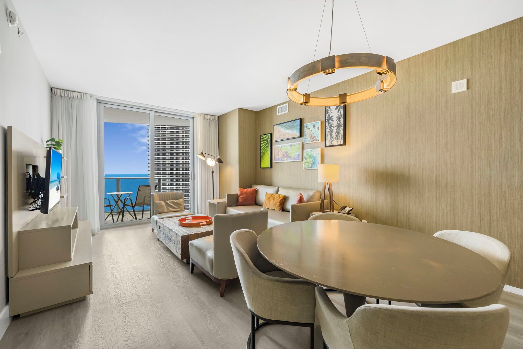 A modern hotel room with a balcony, a dining area with a round table, and a sofa set.