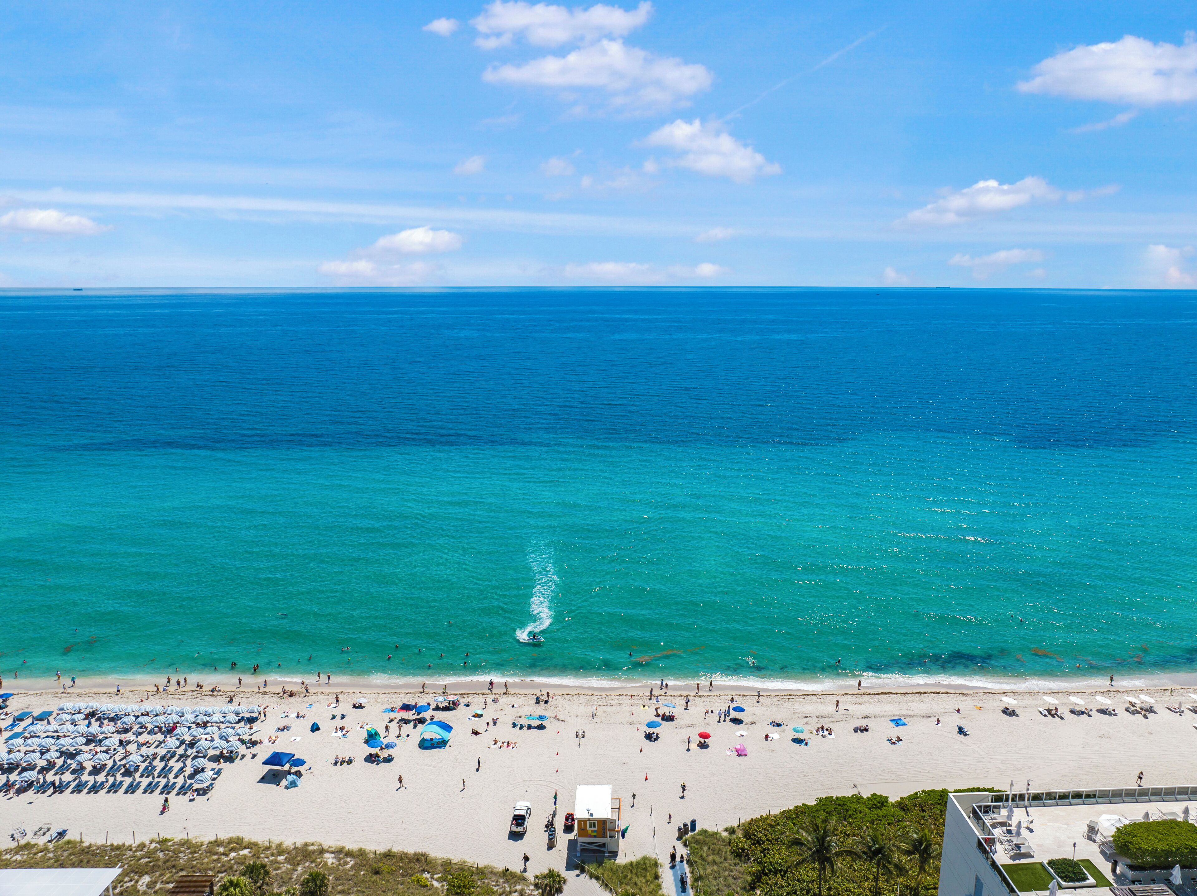 A beach with rows of umbrellas and sun loungers, a clear view of the ocean, and a distant shoreline.