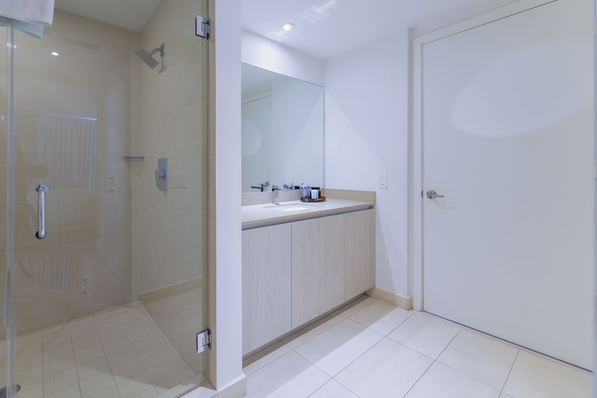 A modern bathroom with a glass shower enclosure, a sink with a mirror, and a door.