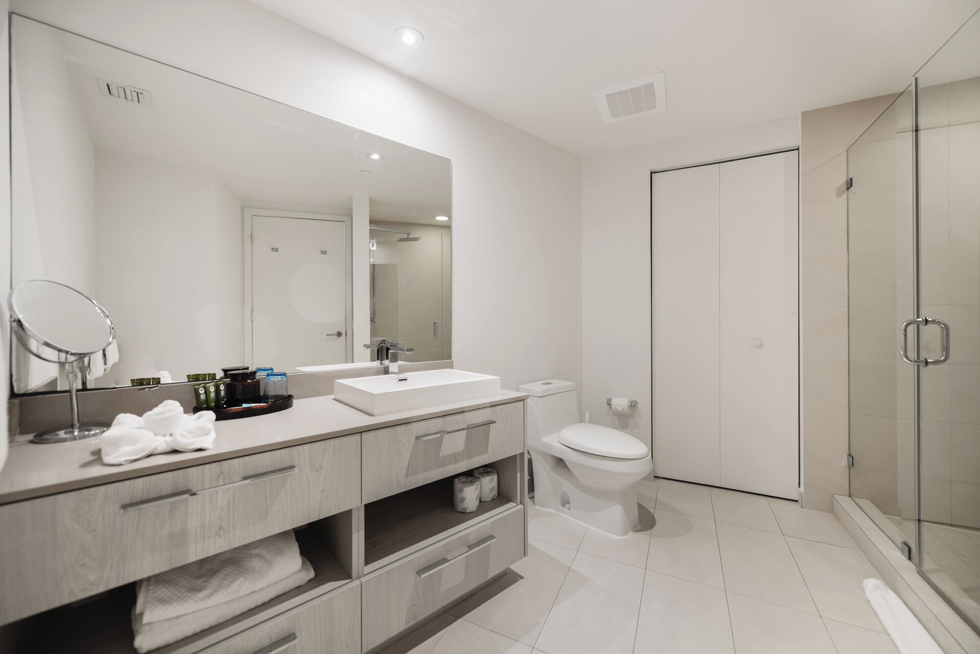 Un baño moderno con un espejo grande, un lavamanos, un inodoro y una cabina de ducha de vidrio.