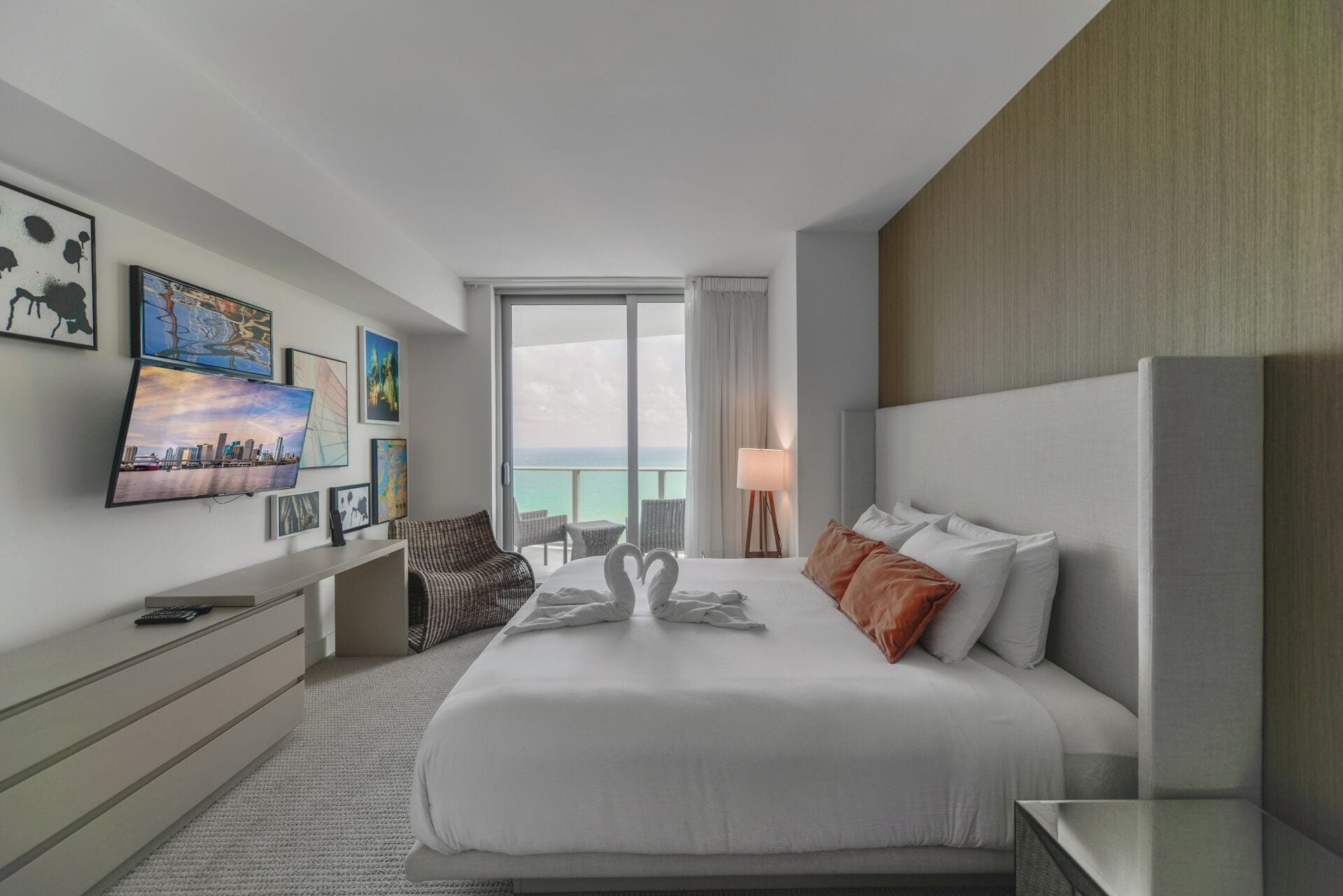 Een hotelkamer met een groot bed, een aan de muur bevestigde televisie en uitzicht op de oceaan door het raam.