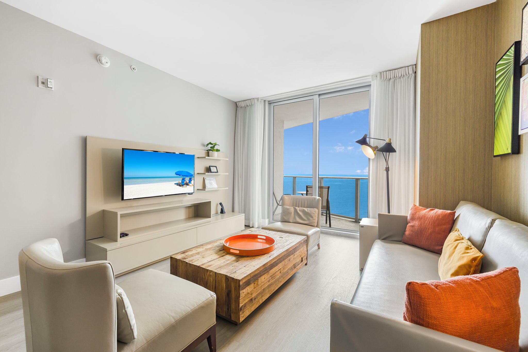 A modern living room with a flat-screen TV, a wooden coffee table, a sofa, and a view of the sea through large windows.