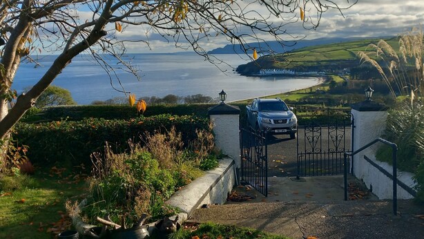 A car parked at a gated entrance with a view of a coastal landscape and a body of water.