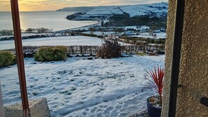 A snowy landscape with a view of the sea and distant hills.