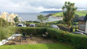 A patio with outdoor seating, a view of the sea, and parked cars.