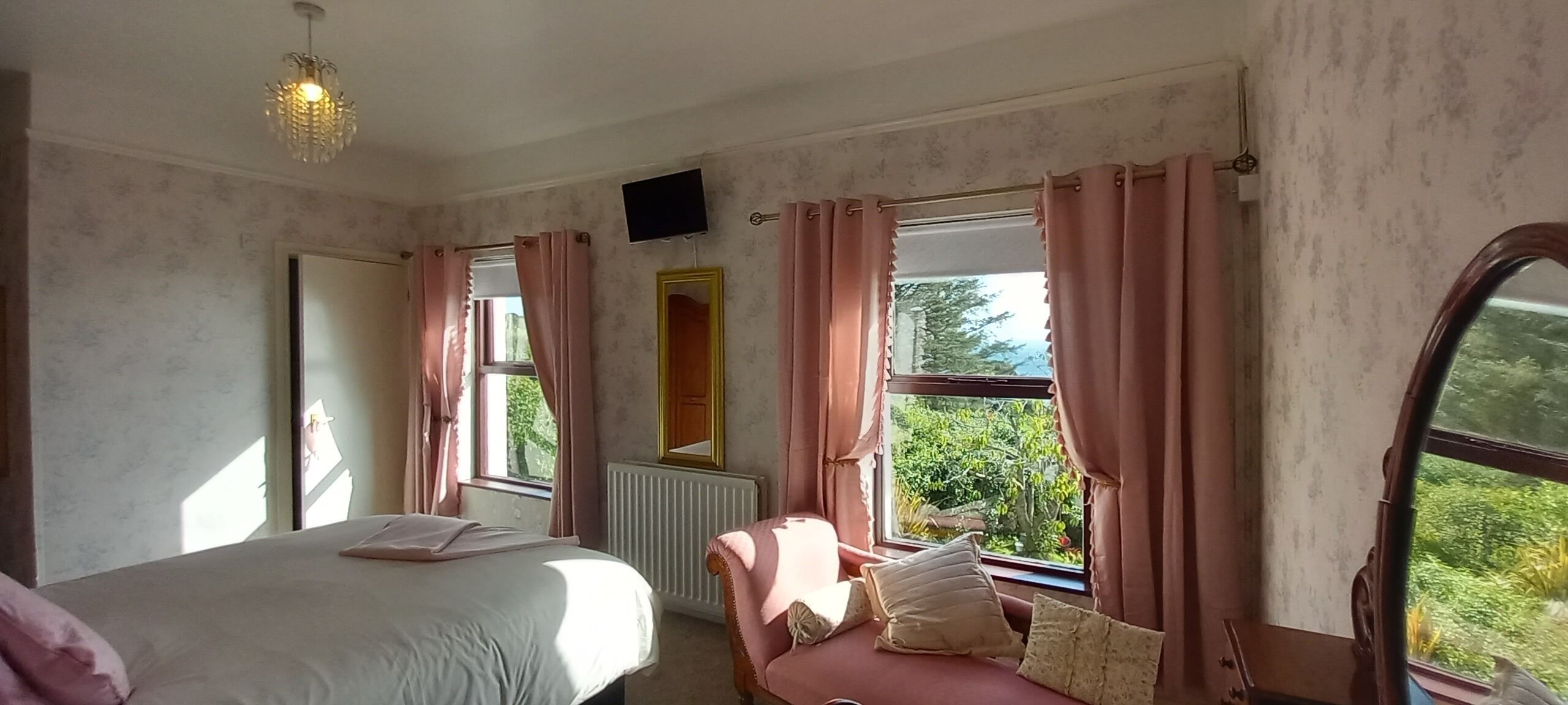 A bedroom with a bed, a window with curtains, a radiator, and a television on the wall.