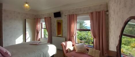 A bedroom with a bed, a window with curtains, a radiator, and a television on the wall.