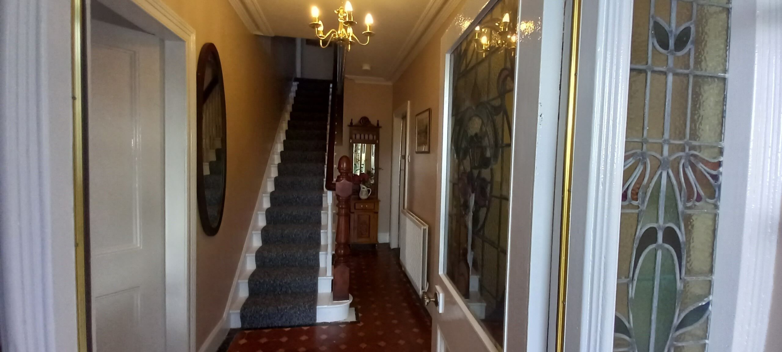 A staircase with a carpeted handrail, a wooden door on the left, and a stained glass window on the right.