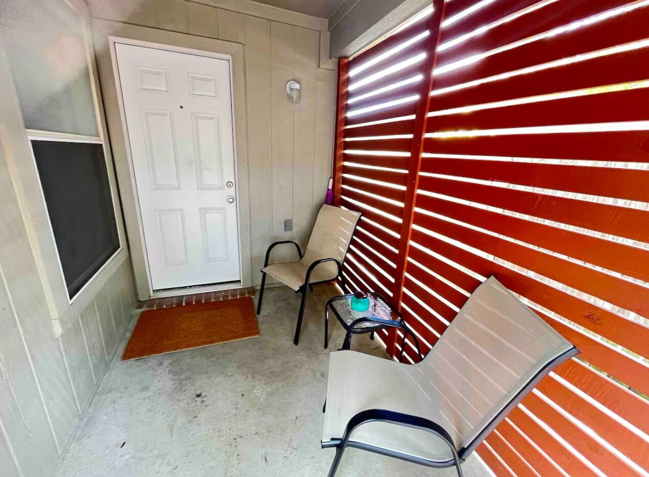 A narrow hallway with a white door, a bench, and a red shuttered wall.