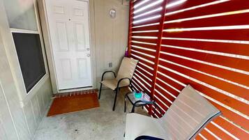 A narrow hallway with a white door, a bench, and a red shuttered wall.