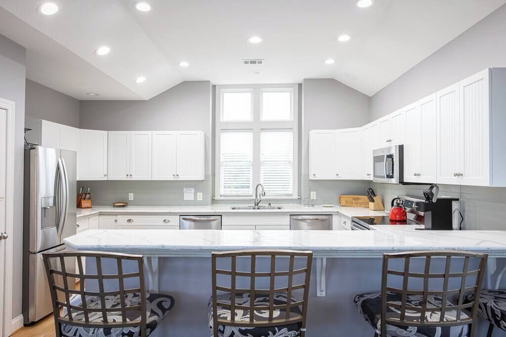 Une cuisine moderne avec des meubles blancs, un îlot central doté de tabourets et des appareils électroménagers intégrés.