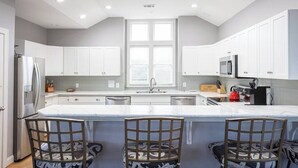 A modern kitchen with white cabinets, a central island with bar stools, and built-in appliances. - Duck Location! Volleyball, Pool, Game Room & More (Duck)
