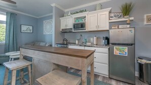 A compact kitchen with white cabinets, a stainless steel refrigerator, a microwave, and a stove. There is a wooden table and two stools. - Cozy Resort - Pickleball, Beaches, Boat Ramps (Huddleston)