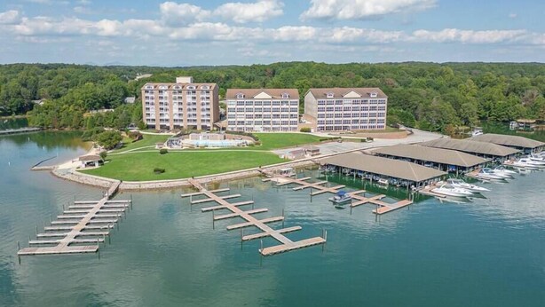 A marina with docked boats, a large building with multiple floors, and a grassy area in front. - Cozy Resort - Pickleball, Beaches, Boat Ramps (Huddleston)