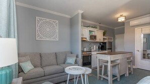 A compact living space with a sofa, a small round table, a kitchenette with cabinets and appliances, and a door leading to another room. - Cozy Resort - Pickleball, Beaches, Boat Ramps (Huddleston)