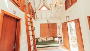 A room with a wooden ladder, a green sofa with floral cushions, a ceiling fan, and a window with a view of the outside. - Ibirawave (Imbituba)