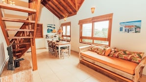 A cozy room with a wooden staircase, a dining area with chairs and a table, a sofa with cushions, and a window with a view. - Ibirawave (Imbituba)