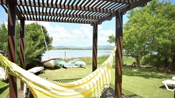 A hammock under a wooden pergola with a view of a lake and boats. - Ibirawave (Imbituba)