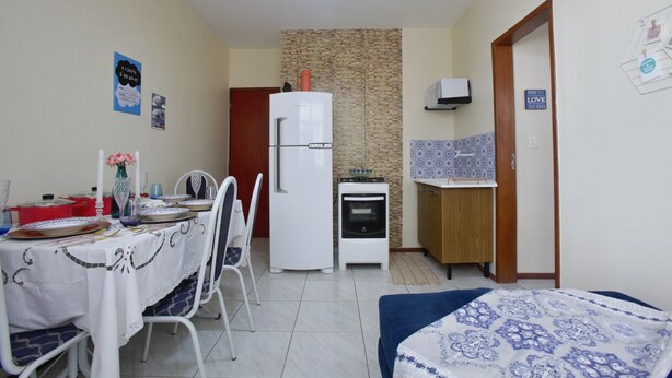 A compact kitchen with a refrigerator, oven, and microwave. There is a dining table with chairs and a small kitchenette area. - Mar Doce Lar (Cabo Frio)