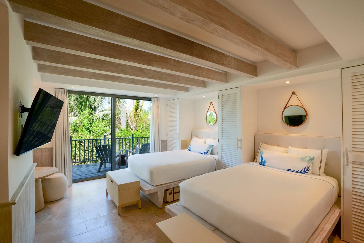 Une chambre d’hôtel avec deux lits, un téléviseur fixé au mur, un balcon donnant sur un espace verdoyant et un plafond en bois.