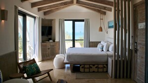Un dormitorio con una cama grande, una banca, un televisor y vistas al mar.