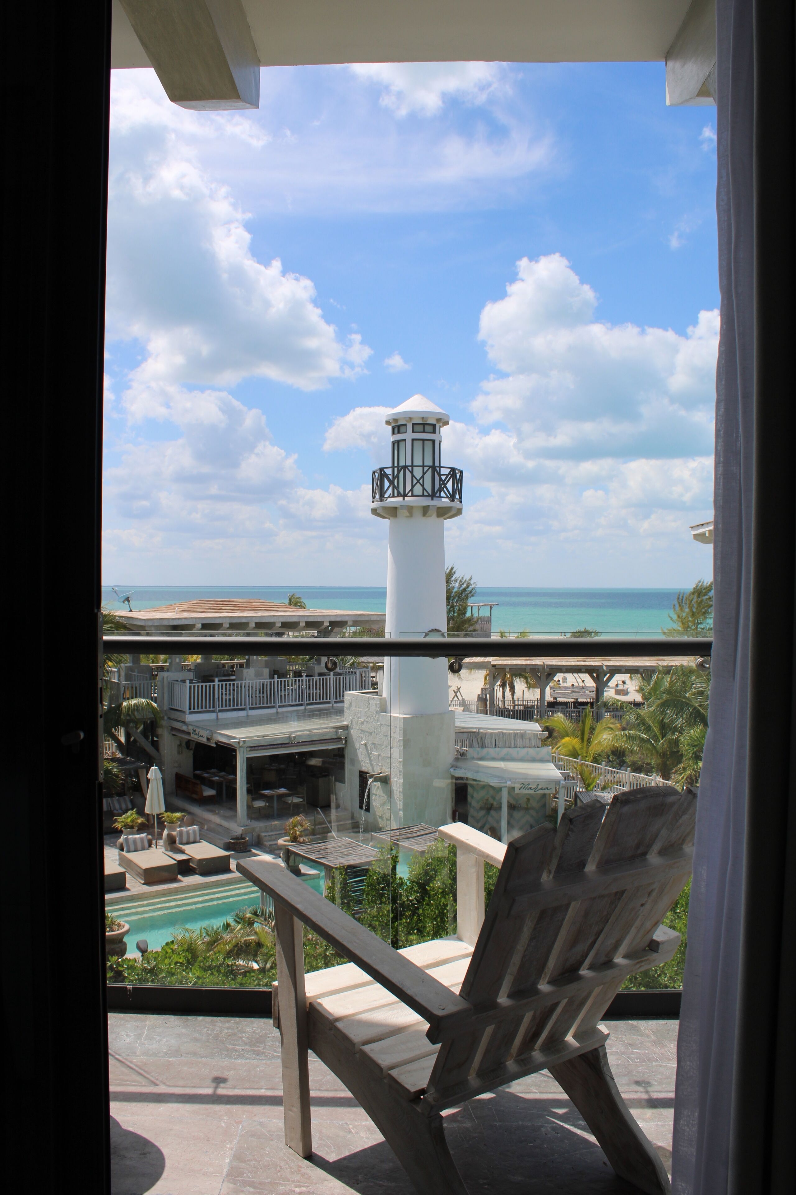 A balcony with a view of a white lighthouse, a pool, and the ocean.