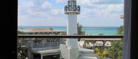 A balcony with a view of a white lighthouse, a pool, and the ocean.