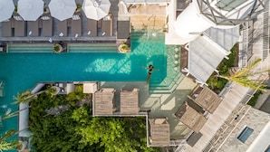 Vista aérea de una zona de piscina en la azotea con sillones, sombrillas y una persona nadando.