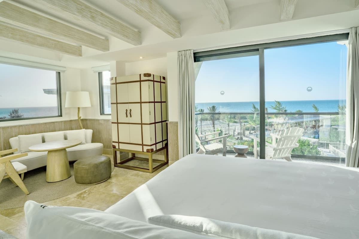 Une chambre d’hôtel avec un grand lit, un canapé, une petite table, une armoire et un balcon donnant sur la mer.