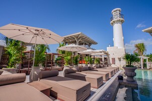 Uma área de estar à beira da piscina, com espreguiçadeiras, guarda-sóis e uma imponente estrutura de farol branco.