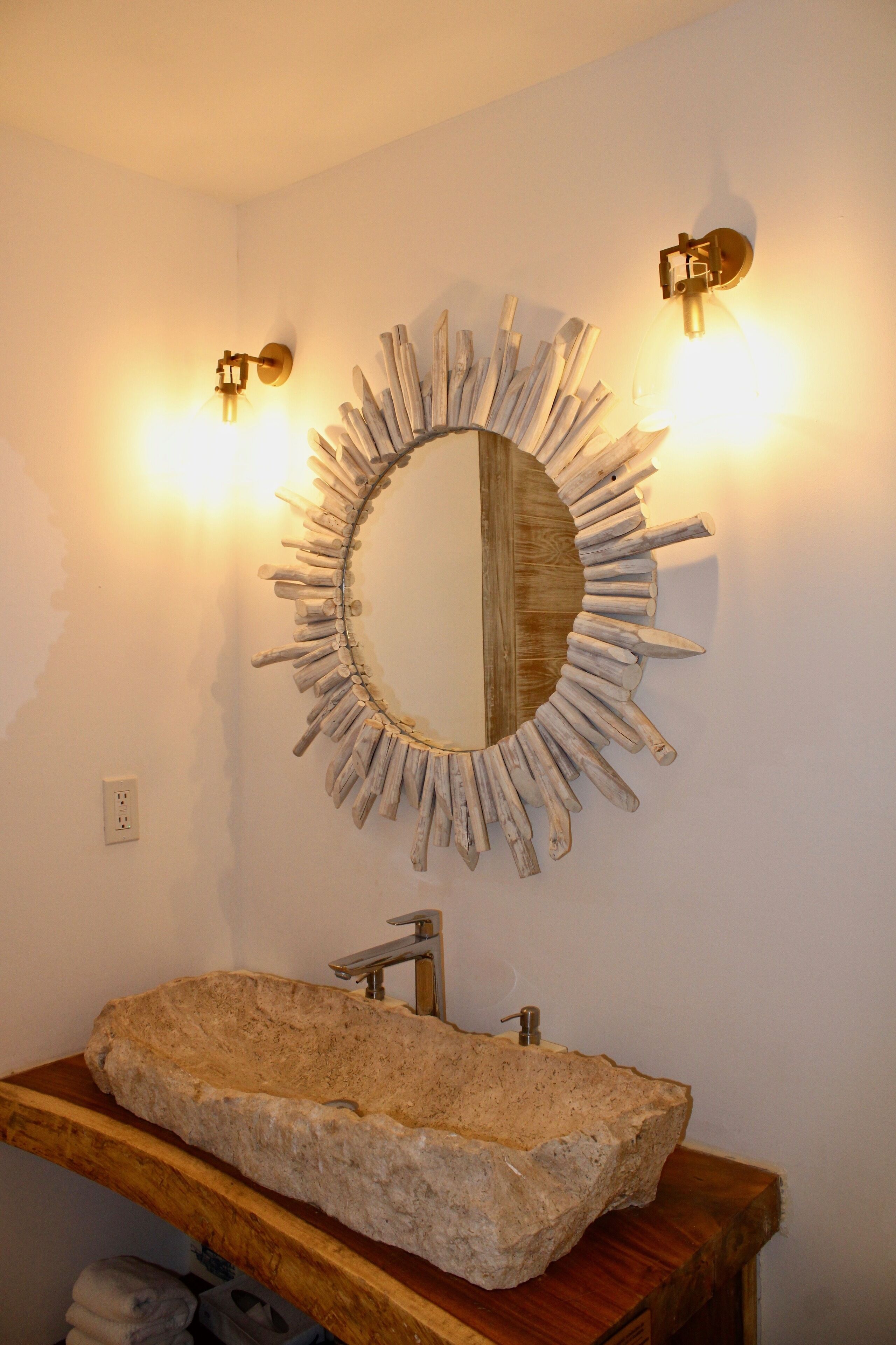 A bathroom with a stone sink, wooden vanity, and a sunburst mirror.