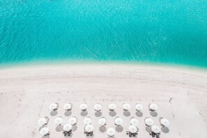 An aerial view of a beach with rows of hexagonal sun loungers and umbrellas, a clear turquoise sea, and a sandy shore. - Delek Holbox (Isla Holbox)