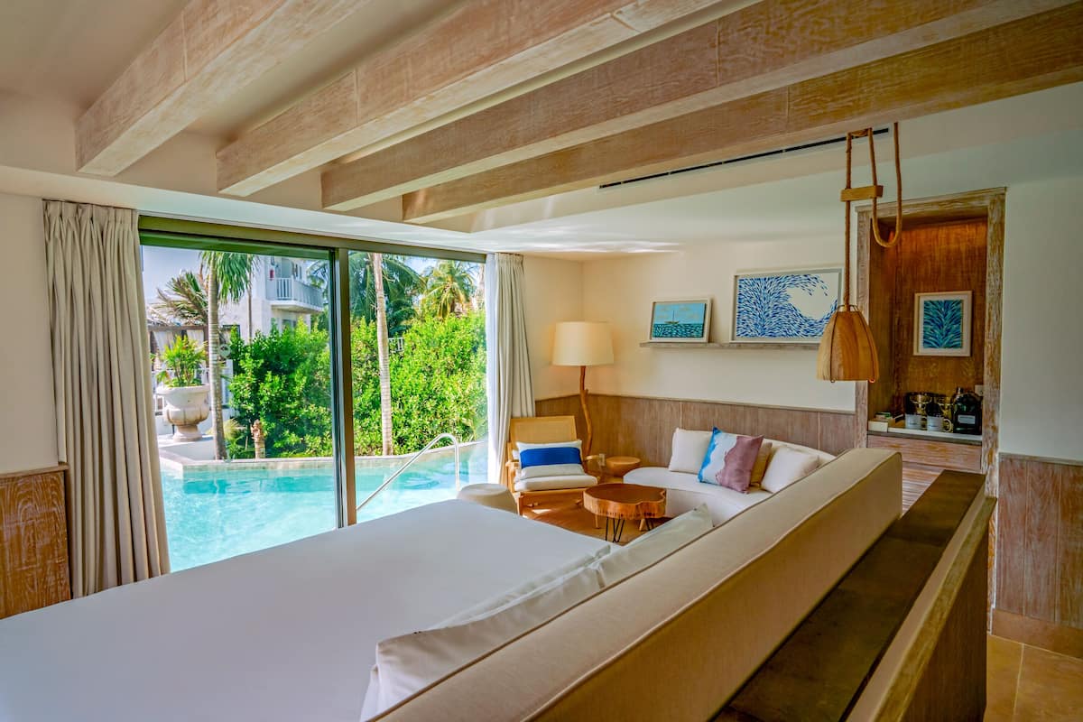 Une chambre d’hôtel avec un grand lit, une petite table, une chaise, une lampe et une vue sur une piscine.