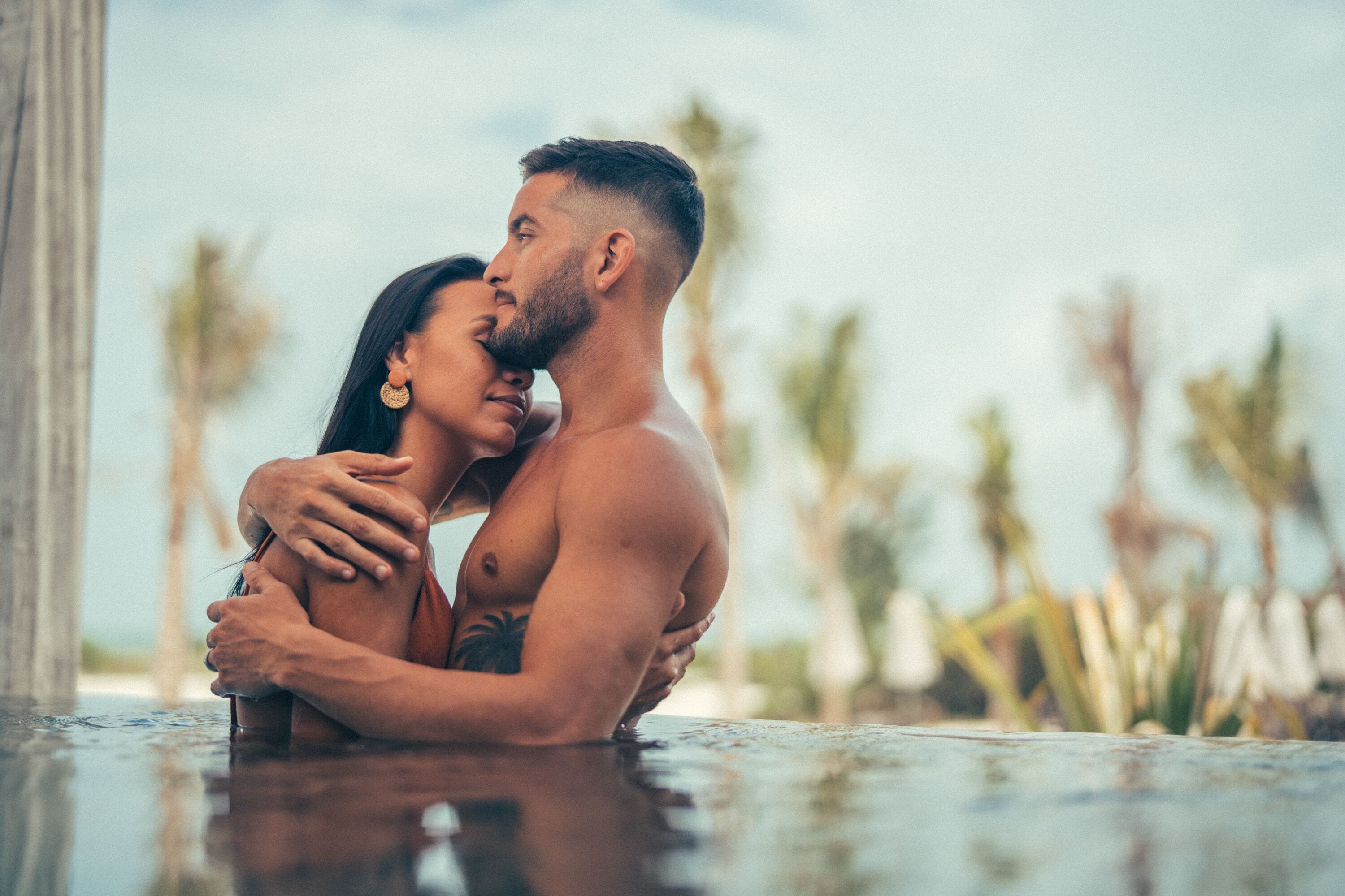 A couple embracing in a pool with palm trees in the background.