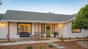 Ein eingeschossiges Haus mit Veranda, einer grünen Tür und einem kleinen Garten mit trittsteinfreiem Zugang.