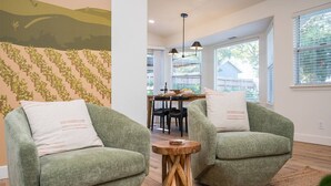 Ein modernes Wohnzimmer mit zwei grünen Sessel, einem Holztisch und einem Essbereich im Hintergrund.