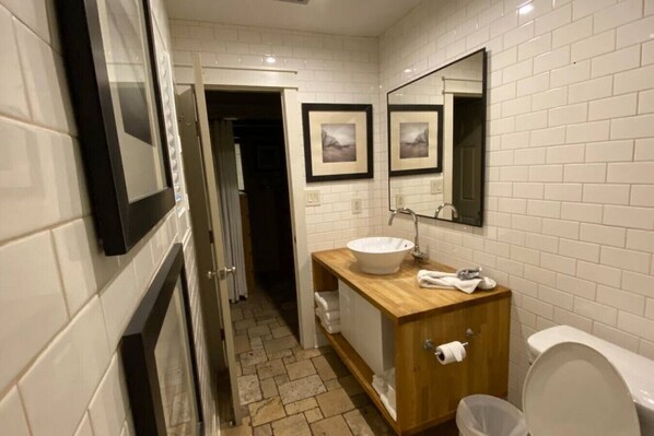 A bathroom with a white tiled wall, a wooden vanity with a sink, a mirror, and a toilet. - Beach Retreat 30A Seagrove (Santa Rosa Beach)
