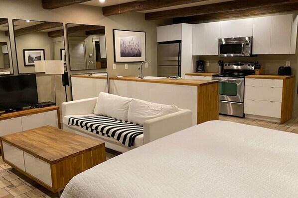 A modern hotel room with a large bed, a sofa with a striped cushion, a wooden coffee table, a TV, a kitchenette with a microwave, stove, and refrigerator, and a large mirror. - Beach Retreat 30A Seagrove (Santa Rosa Beach)