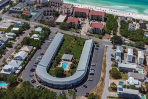 Vue aérienne d’un hôtel situé sur la côte, avec un bâtiment aux lignes courbes, des parkings et une plage en arrière-plan.