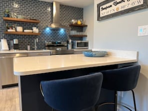A kitchen with a central island, two bar stools, and a sign indicating the address.