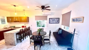 Una cocina moderna con armarios oscuros, una zona de comedor con suelo de mármol, un ventilador de techo y un sofá negro.