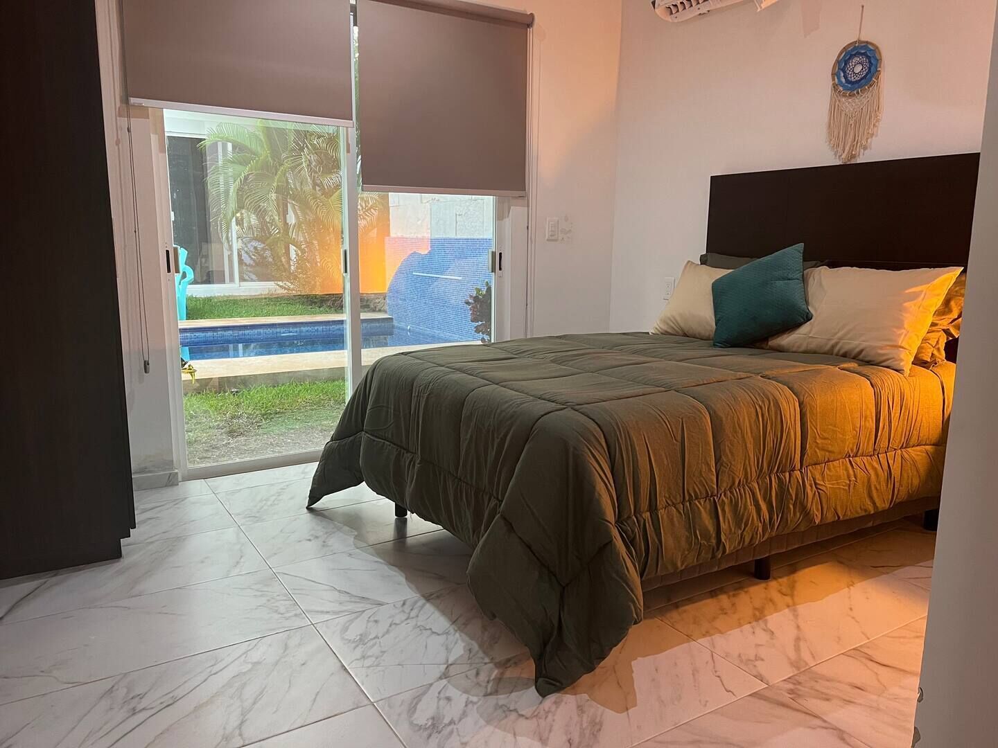 A bedroom with a bed, a sliding glass door leading to a pool, and a dreamcatcher on the wall.