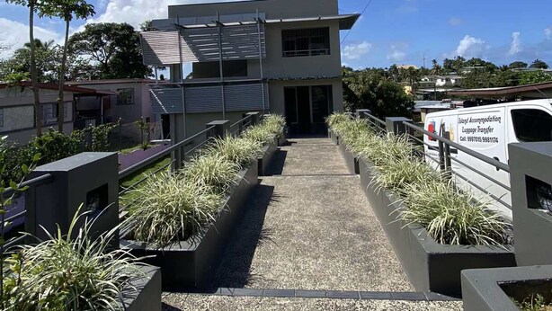A modern building with a pathway leading to the entrance, surrounded by planters with greenery. - Island Travelers Acccommodation (Suva)