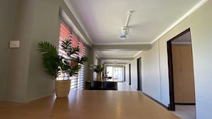 A long, narrow hallway with a wooden reception desk, potted plants, and a ceiling fan. - Island Travelers Acccommodation (Suva)