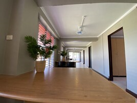 Un pasillo largo y estrecho con una recepción de madera, plantas en macetas y un ventilador de techo.