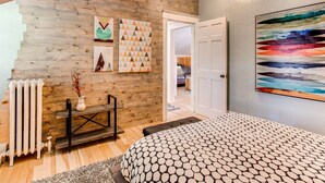 Une chambre avec un mur en bois, une grande peinture abstraite et une couvre-lit à motifs.